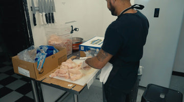 employee working hard cutting chicken and prepping it to be tossed into a fryer